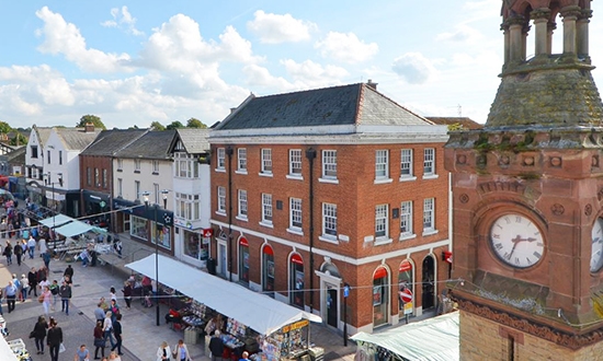 Overhead view of Ormskirk town center, featuring historic buildings, shops, and a bustling market square with pedestrians and local vendors.